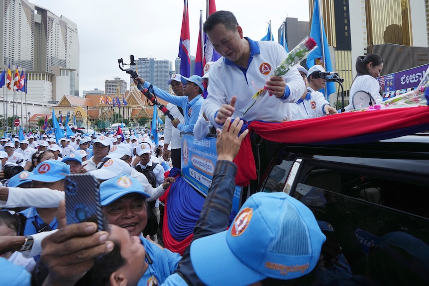 Cambodian People's Party's Hun Manet accepts a rose from the crowd from the back of a pick-up truck.
