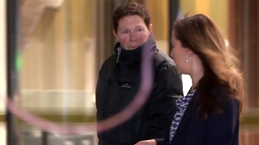 A woman with short hair and wearing a puffer jacket walks alongside a female lawyer at night.