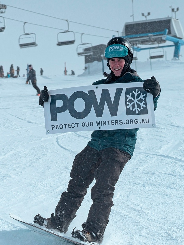 A snowboarder holding up a sign saying POW