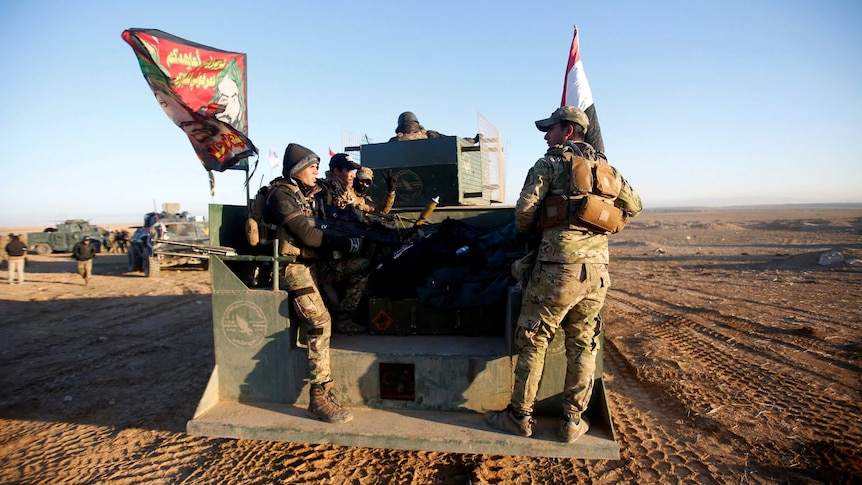Soldiers sit in the back of a truck holding Iraqi flags