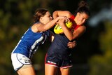 Melbourne Football Club AFLW player Libby Birch struggles to hold onto a yellow football while being tackled by another player