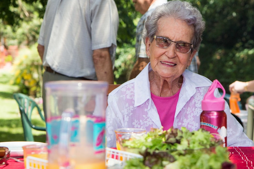Image of an elderly woman sitting at a picnic table.