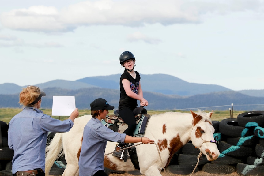 Girl rides horse while teachers hold up signs.