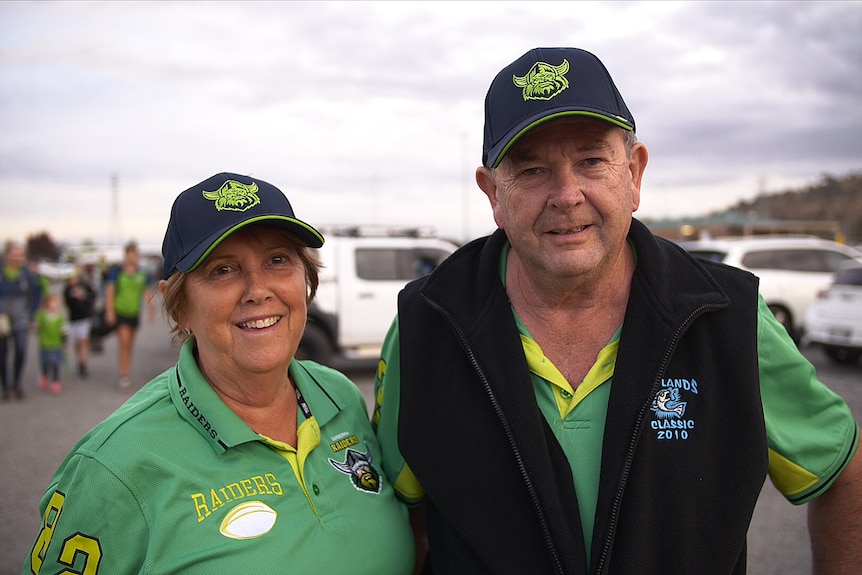 Two people in Canberra Raiders merchandise smile at the camera