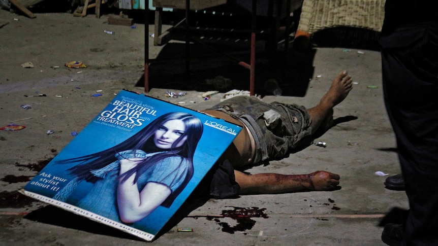 Police investigators used a poster to cover the body of an unidentified male victim shot in Quezon City.