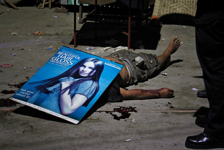 Police investigators used a poster to cover the body of an unidentified male victim shot in Quezon City.