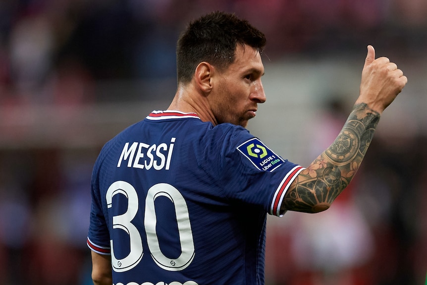 Lionel Messi, wearing a PSG jersey, turns and gives a thumbs up