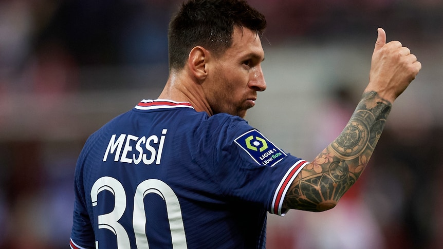 Lionel Messi, wearing a PSG jersey, turns and gives a thumbs up