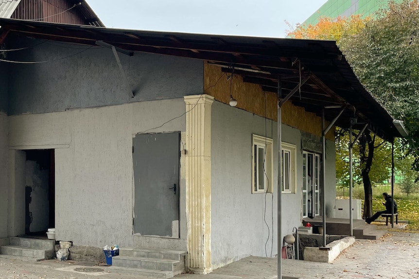 A house painted grey with a man sitting on a chair in the background.