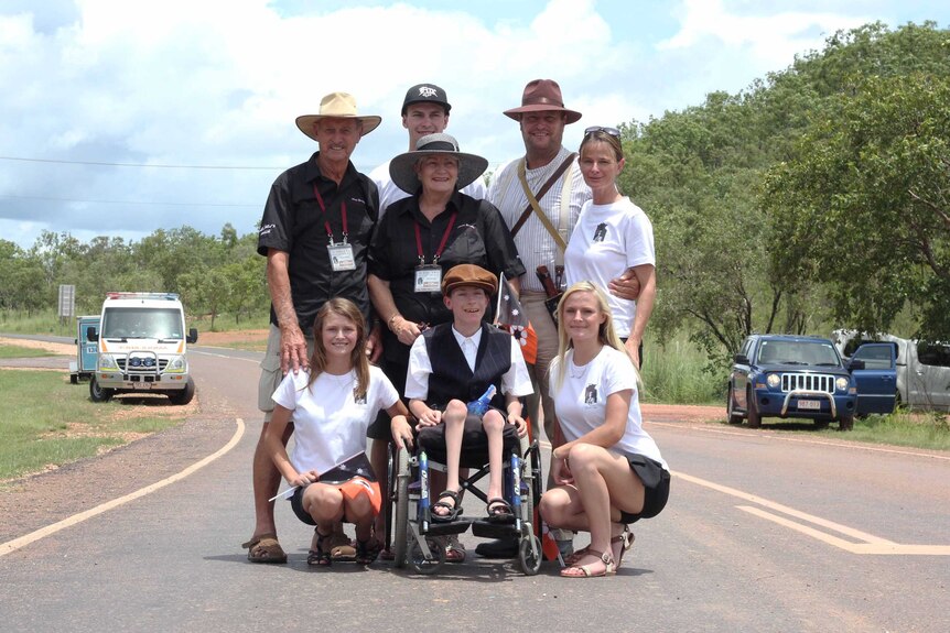 A group of young and old people stand together on a road.