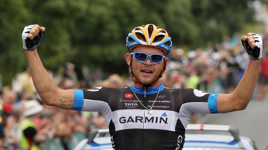 Bobridge, on a bicycle, raises his arms in a victory gesture.