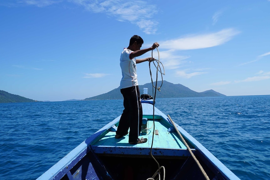 A fisherman stands on a boat in the middle of the sea surrounded by islands