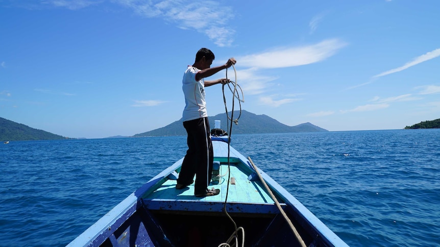 A fisherman stands on a boat in the middle of the sea surrounded by islands