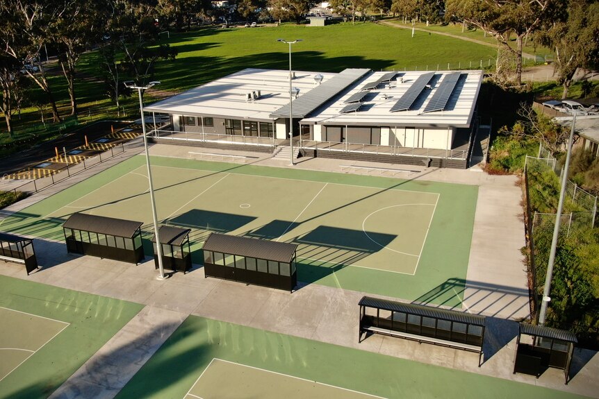 Three netball courts in foreground, club rooms in background, flanked by green space