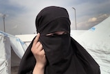 A woman in a hijab looks off while standing in a UNHCR refugee camp