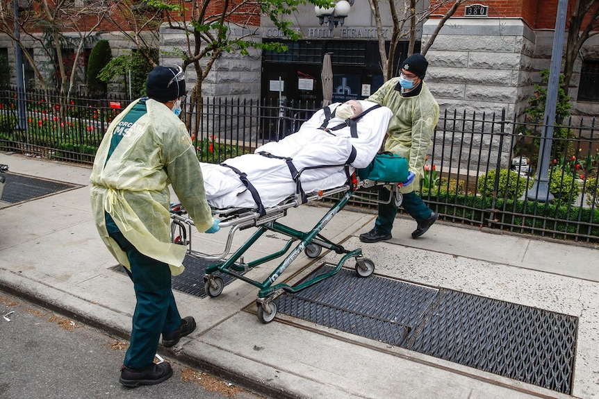 A patient in a stretcher is being loaded into the back of an ambulance by emergency workers.