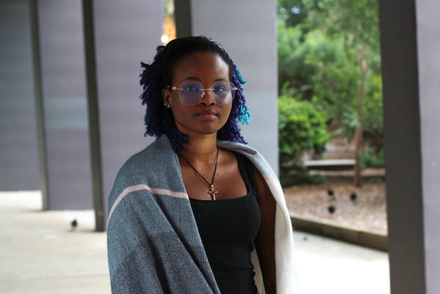 A young woman wears a shawl over her shoulders standing under a covered exterior walkway on a grey day.