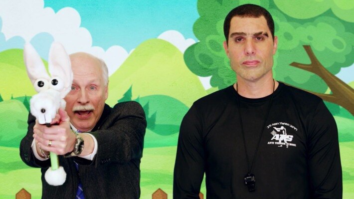 a man in a suit pointing a rabbit gun next to a taller man in a black shirt