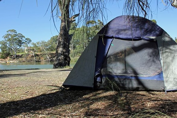 A tent on a river bank with a river in the background. 