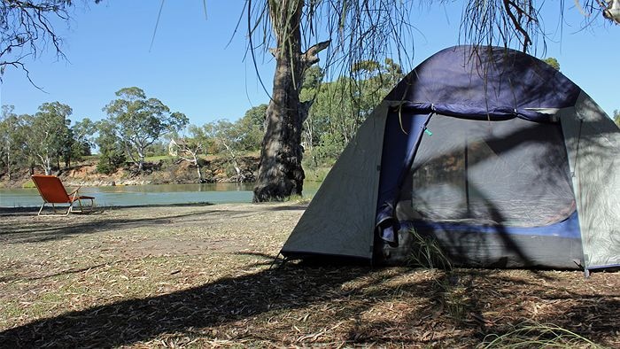A tent on a river bank with a river in the background. 