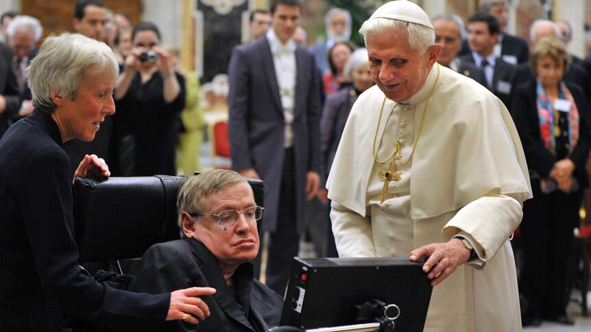 Stephen Hawking looks at his screen with Pope Benedict standing next to him.