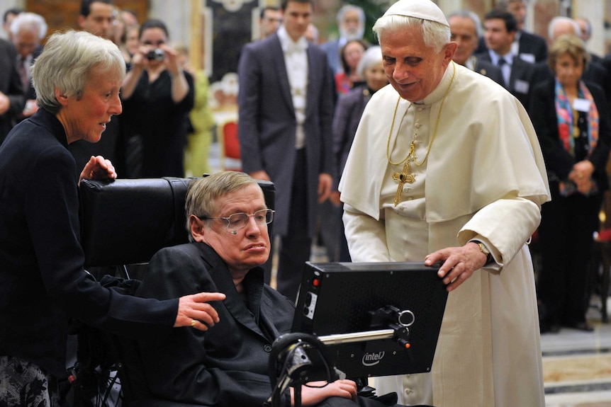 Stephen Hawking looks at his screen with Pope Benedict standing next to him.