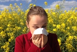 A woman sneezing into a tissue in a field of flowers