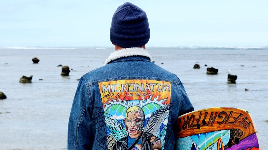 Jeremy Ievins looking out at the sea from the shore, wearing his Mick Fanning painted jacket