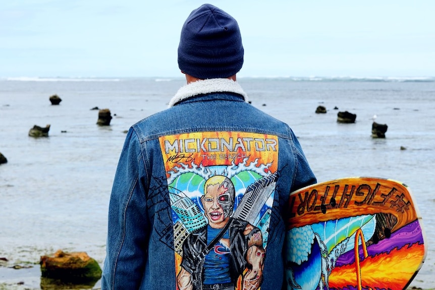 Jeremy Ievins looking out at the sea from the shore, wearing his Mick Fanning painted jacket