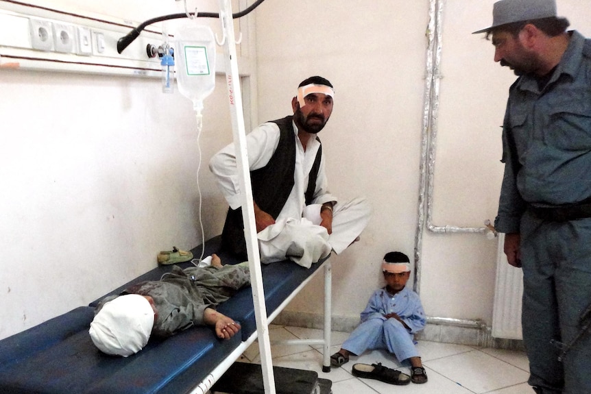 An Afghan policeman looks at a wounded man and children after a suicide attack in Khost city.