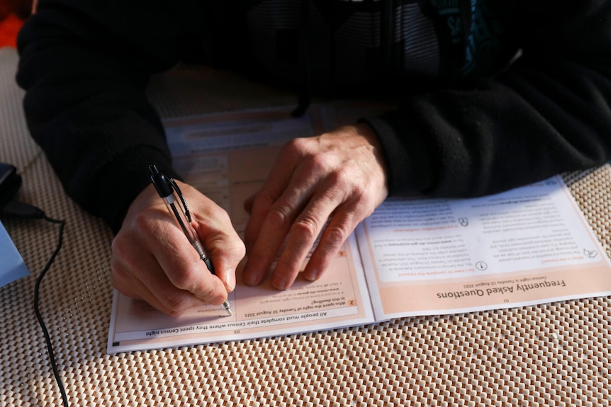 A man holds a pen and fills out the front page of his census form.