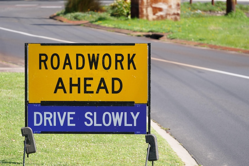 A sign saying roadworks ahead, drive slowly on the side of a road.