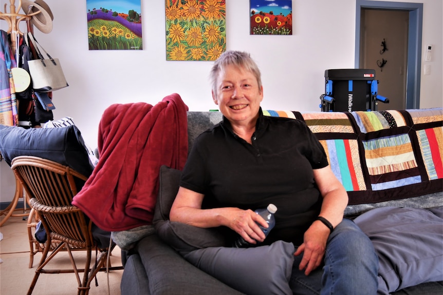 A woman with short grey hair sits smiling on her couch.