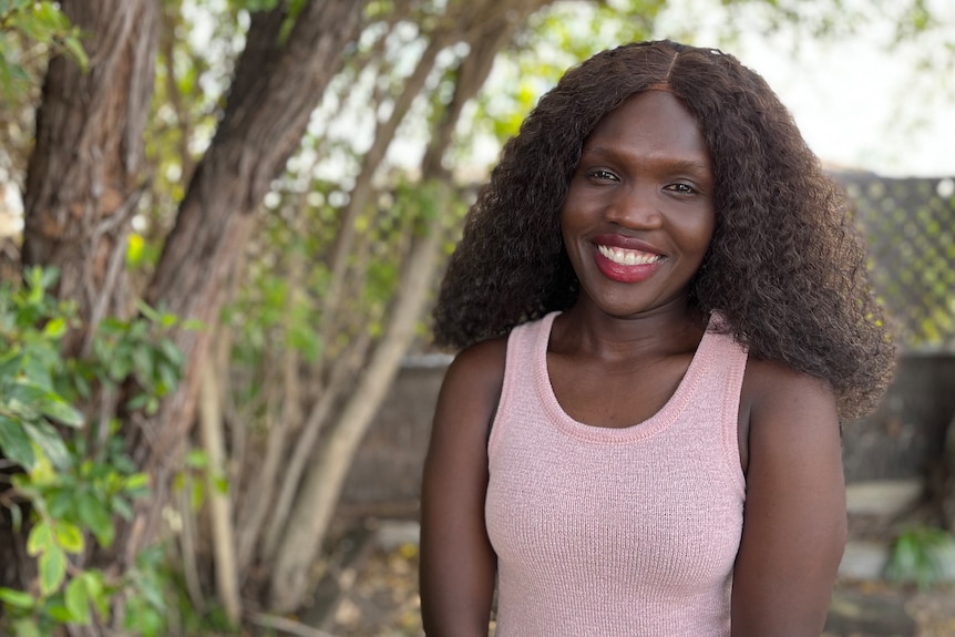 A young woman smiles while standing under a tree