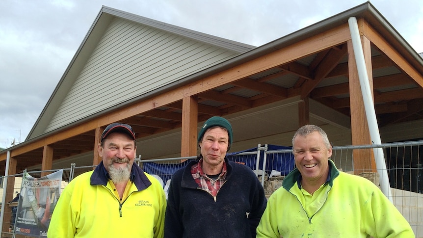 Three men, wearing high-viz jumpers, stand in front of the soon-to-be-completed Buchan Hotel