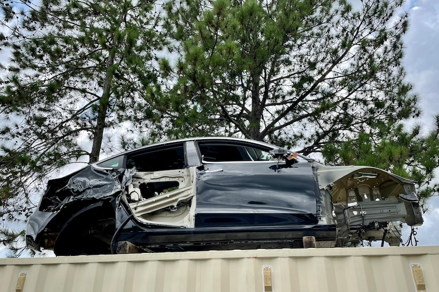 A damaged Tesla car on top of a shipping container.