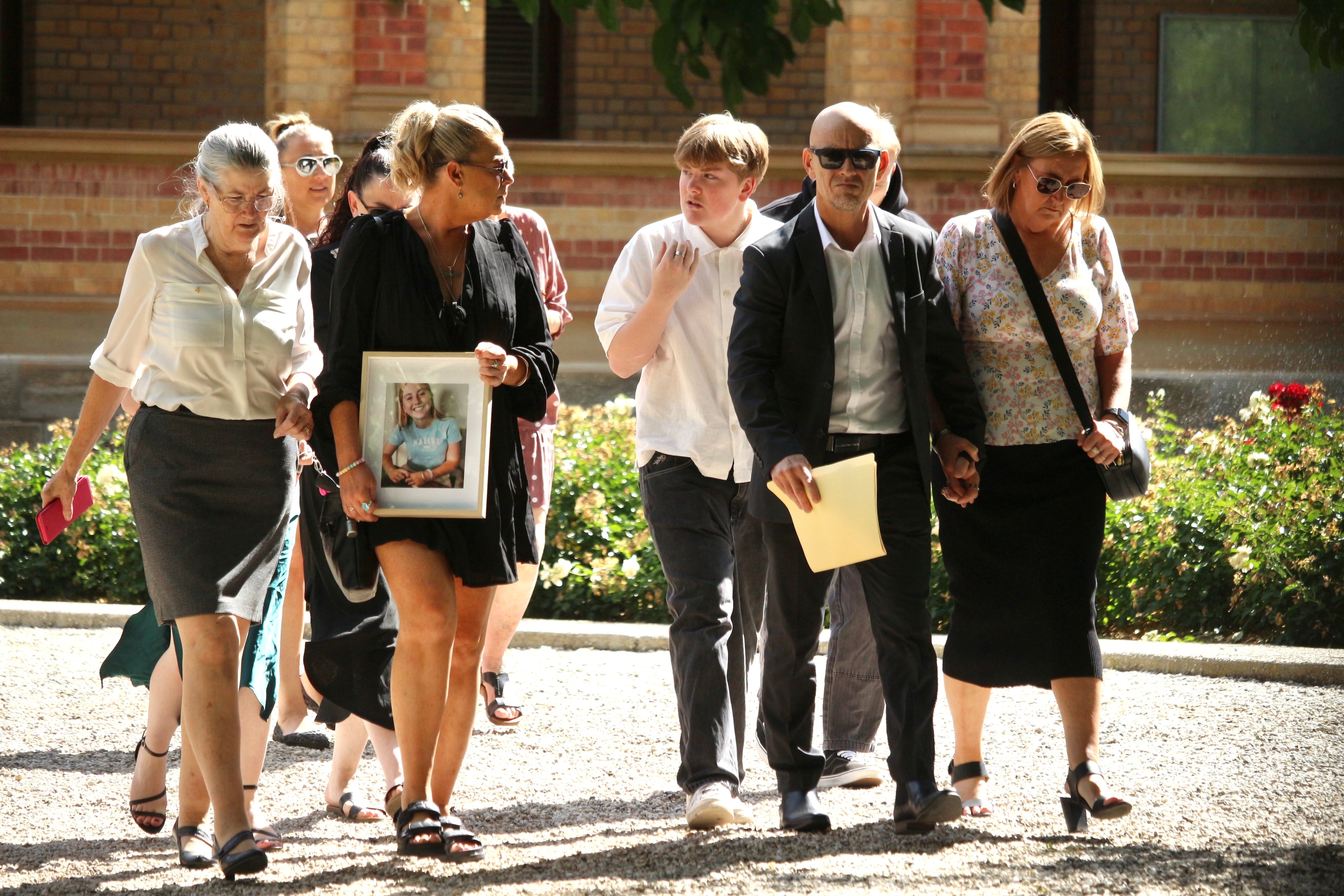 Un grupo de nueve personas de diferentes edades salen juntas de un juzgado, una de ellas con una fotografía enmarcada de una mujer joven.