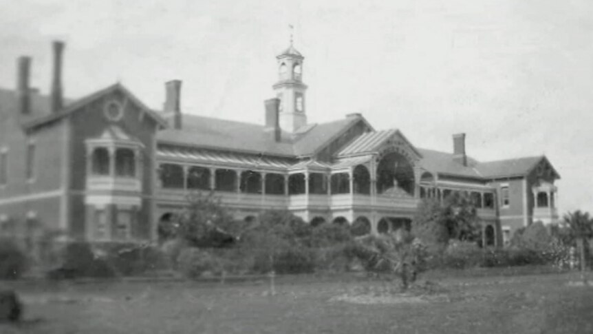 A black and white photo of a large Victorian-era building with wide lawns and garden