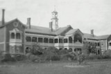 A black and white photo of a large Victorian-era building with wide lawns and garden