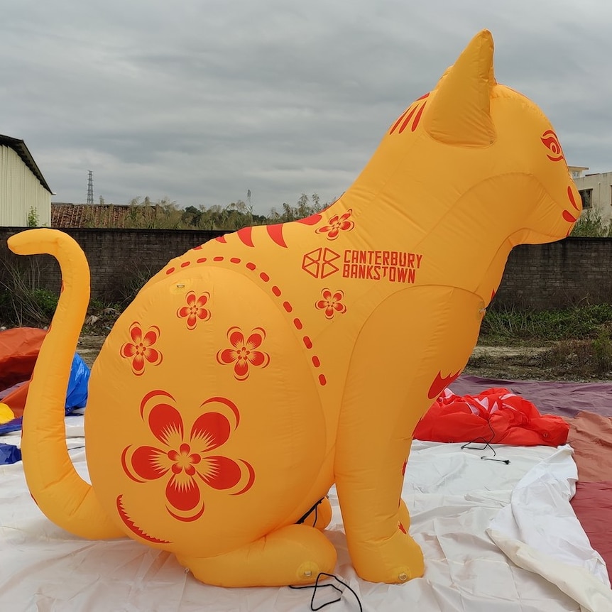A giant inflatable yellow cat with red floral pattern on it. 