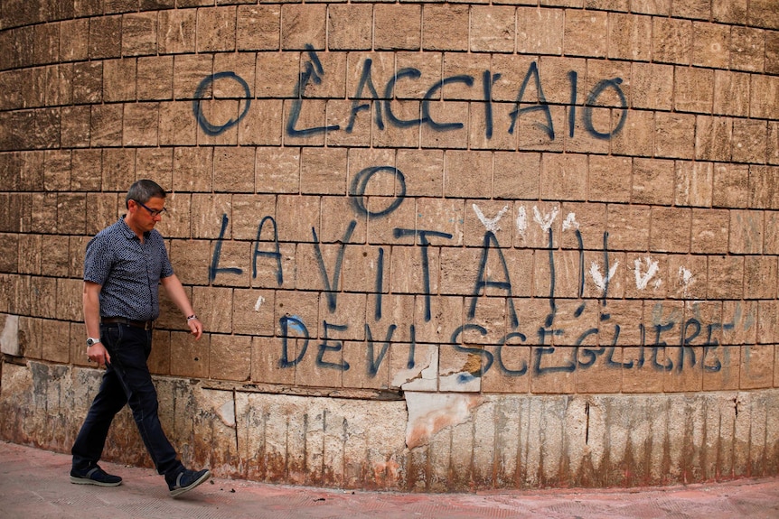 A man walks past a graffiti reading "Steel or life, you have to choose" in Taranto.