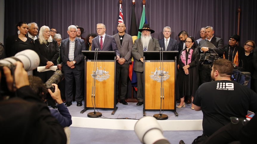 Anthony Albanese stands behind a lecturn flanked by First Nations politicians and experts. 