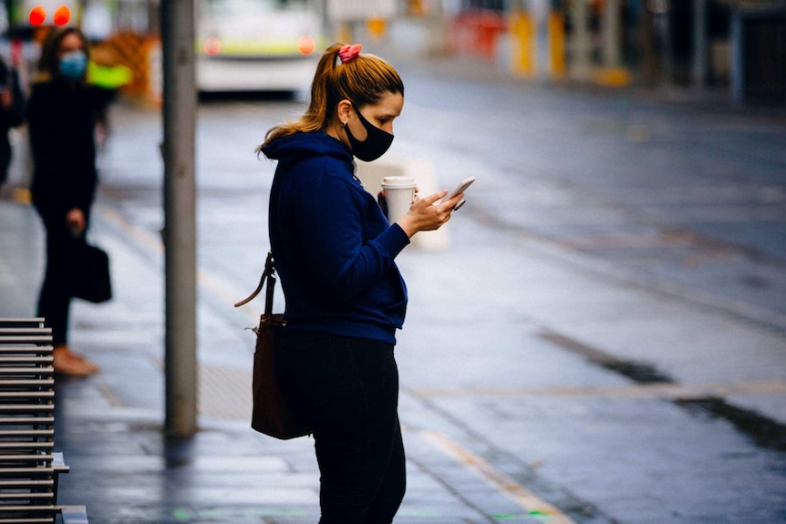 A woman wearing a face mask looks at her phone.