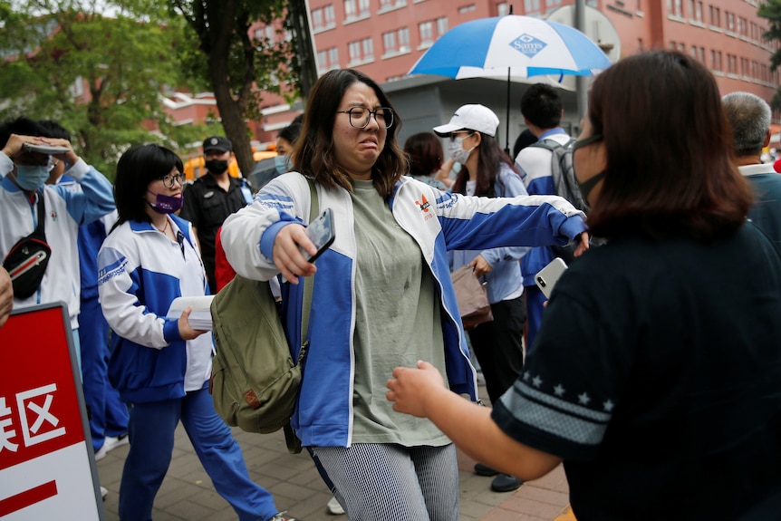 An emotional student approaches a family member with her arms out wide ready for a hug after an exam.