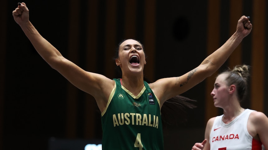 Basketball player Alex Wilson, in a green jersey, raises her hands abover her head in celebration