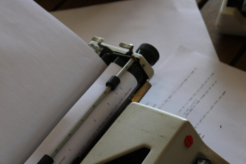 Looking closely at a typewriter with its paper curled around the top cylinder. Gibberish words are printed on the paper.