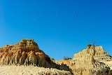 Bright blue sky with three birds flying and orange sandstone dune formations