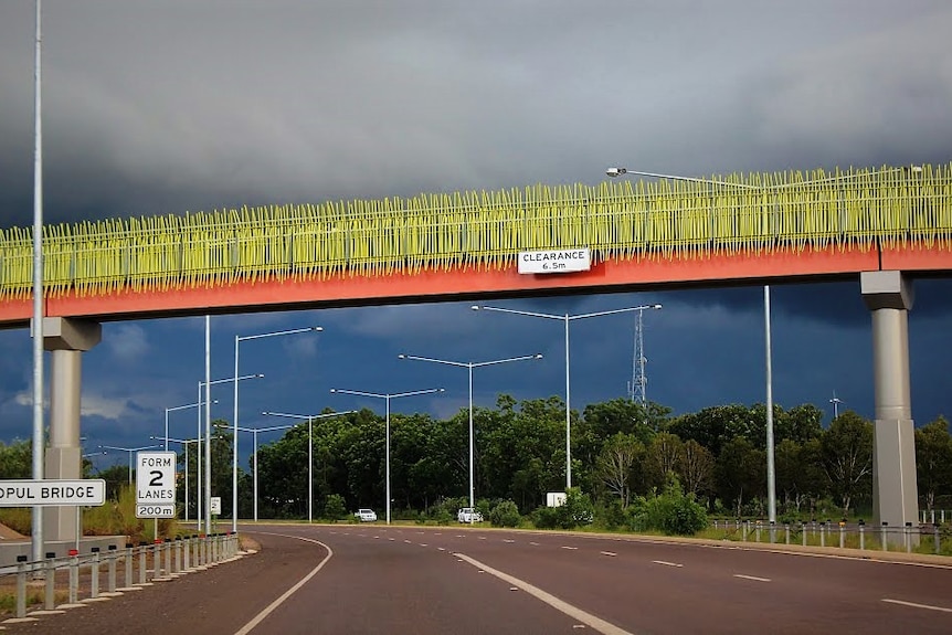 A bright green footbridge over a motorway on a stormy day.