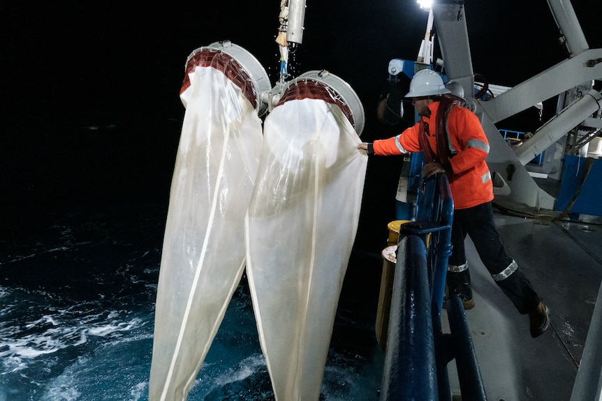 Un uomo tiene grosse reti bianche dal lato della nave