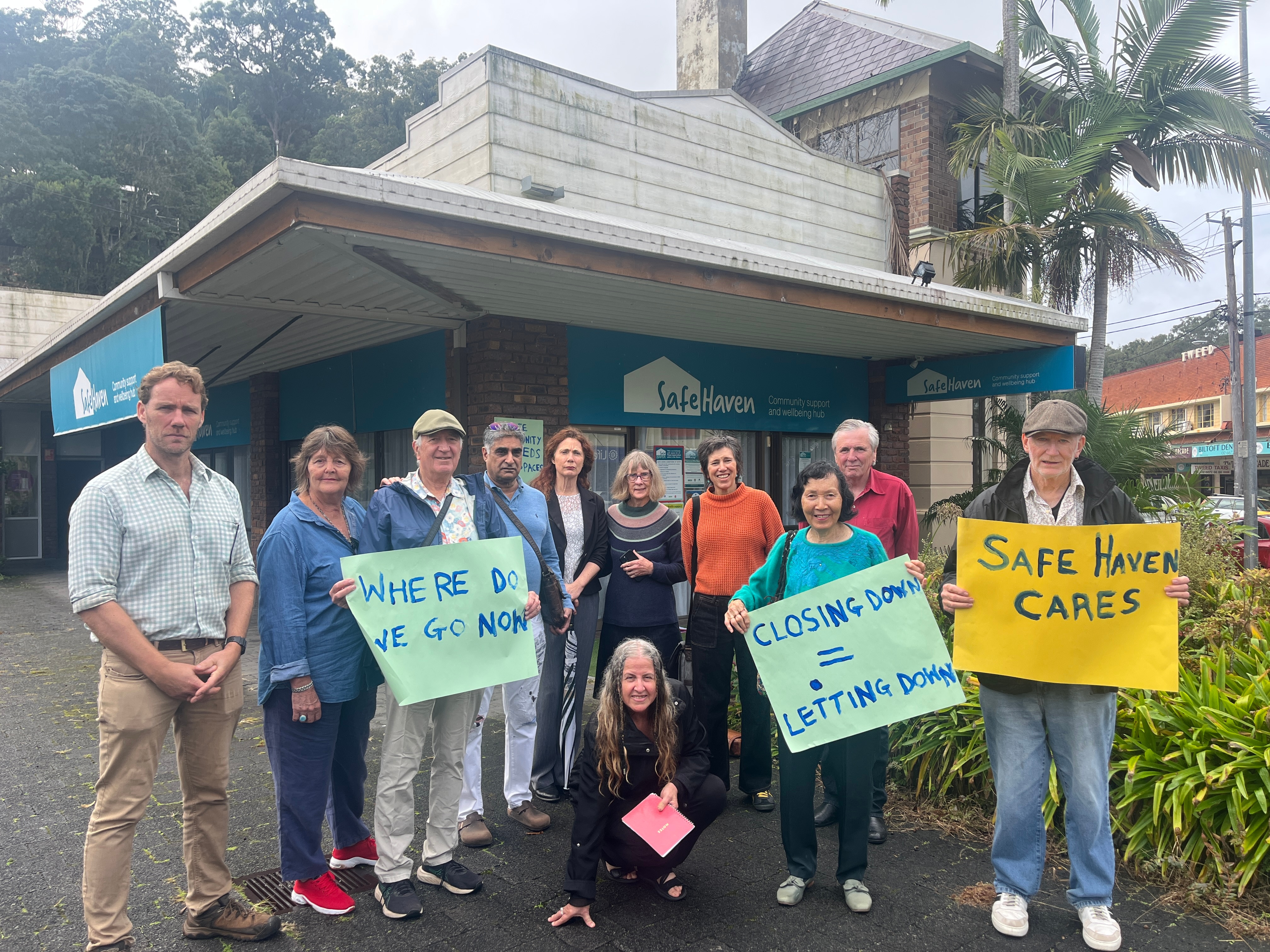Eleven people gather outside Safe Haven Murwillumbah holding signs to protest the mental health service closure.